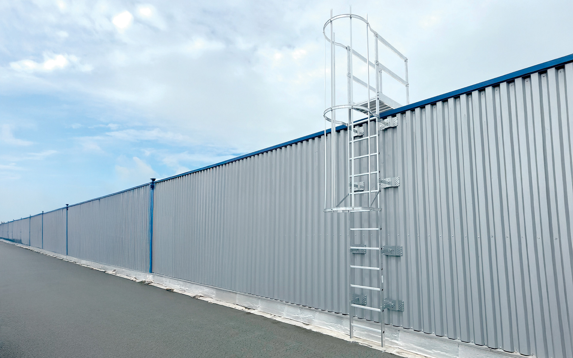 aluminum safety ladder with cage installed on an industrial metal wall