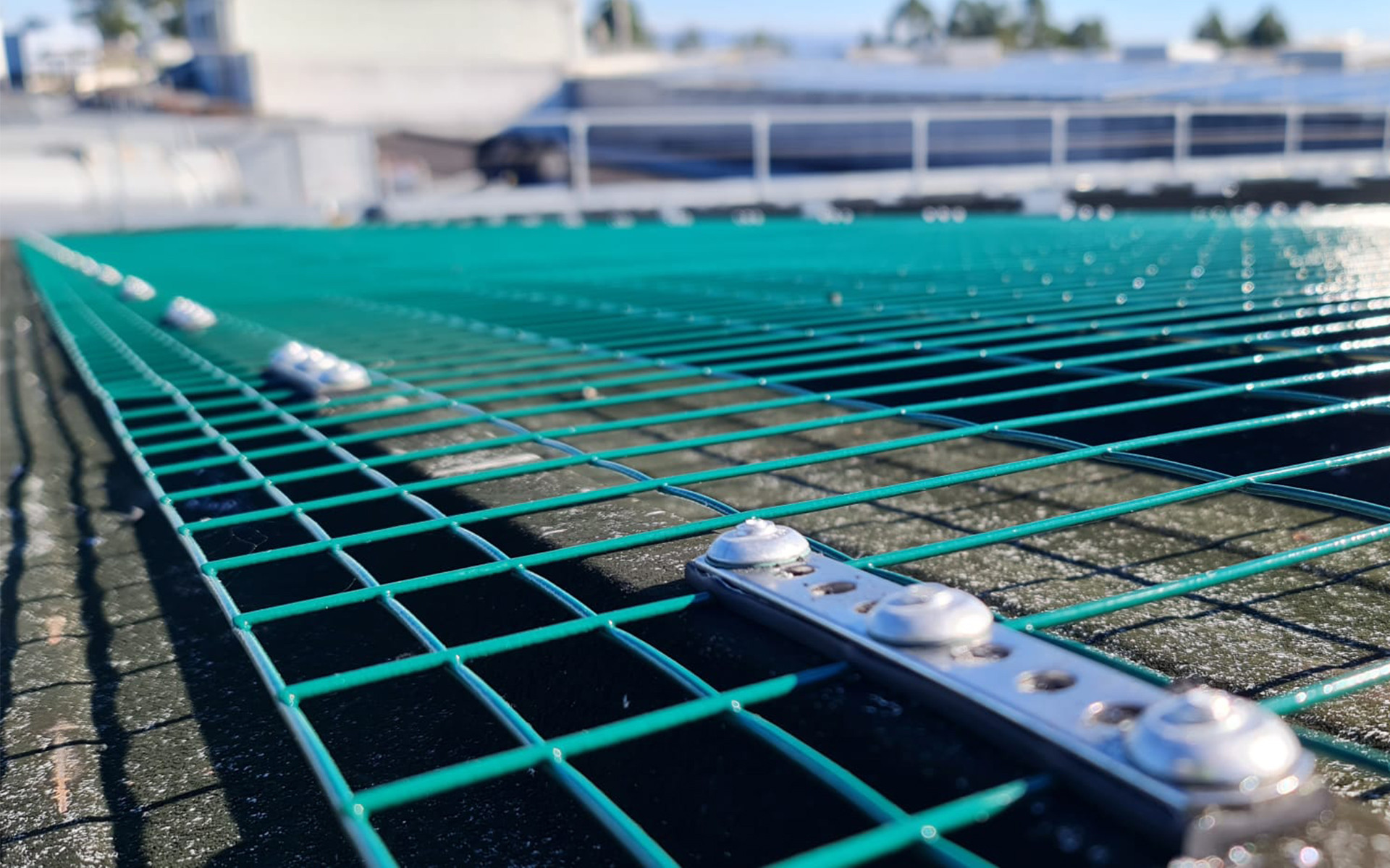 Green safety net installed on a rooftop with secure fastening system. 